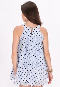 Ljusblå prickig klänning med ett flerradigt mönster, halterneck och knappdetalj bak. Svarta prickar kontrasterar mot tyget.