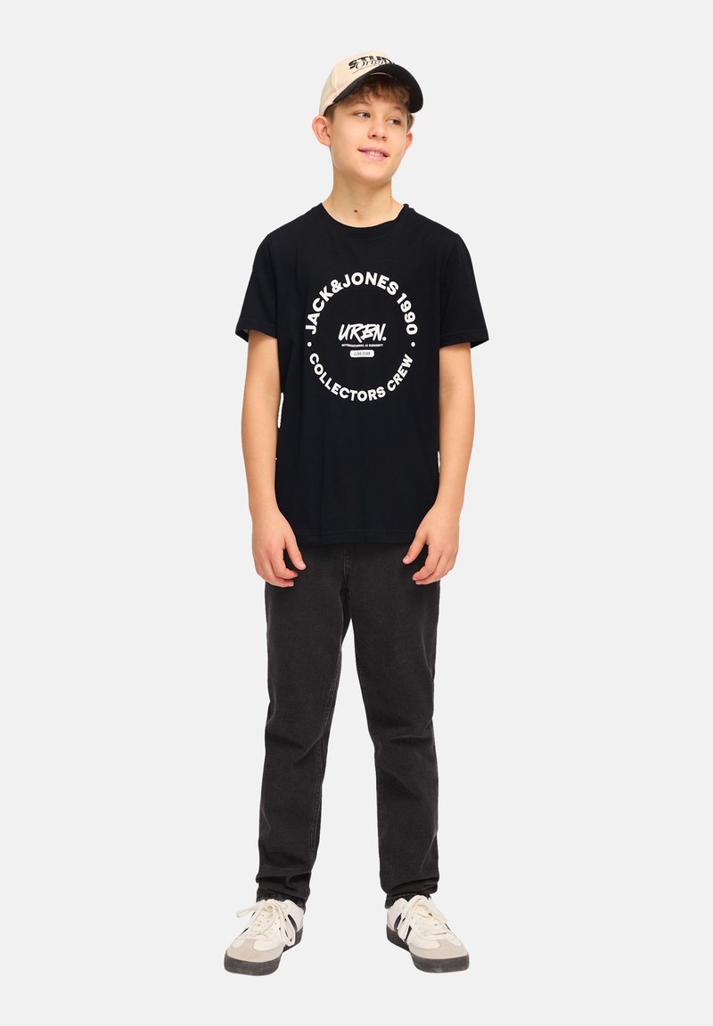 Camiseta negra con estampado gráfico blanco, jeans negros y gorra beige. Los zapatos son una mezcla de blanco y gris. Diseño simple y casual.