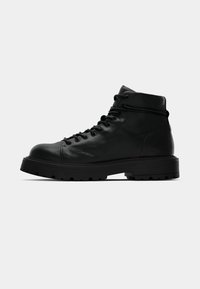 Bottes mi-hauteur en cuir noir à lacets avec col rembourré, semelle en caoutchouc épaisse et semelle à crampons, présentées en profil latéral sur fond blanc.