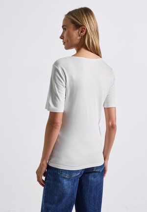 Ljusgrå kortärmad topp med rundad halsringning, slät textur och figursydd silhuett, tillsammans med blå denimbyxor.