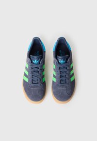 Modro-zeleni Adidas supergi iz semiša z tremi zelenimi črtami, teksturiranim temno sivim zgornjim delom in gumijastim podplatom barve gume.