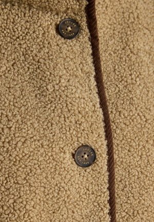 Beige textured fabric coat with a fuzzy outer layer, featuring dark brown accents and a large button labeled "JOULES EST. 1868."