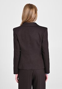 Blazer marrone su misura con una vestibilità strutturata, rever a punta, tessuto testurizzato e spalle strutturate; abbinato a pantaloni coordinati.