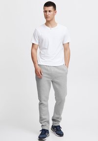 Weißes Baumwoll-T-Shirt kombiniert mit grauer Jogginghose. Die Hose ist an den Bündchen gerippt, und die Person trägt marineblaue Sportschuhe.