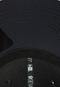 Schwarze Kappe aus glattem Stoff mit mehreren genähten Linien auf dem Schirm. Verfügt über ein strukturiertes Innenband und angehängte Etiketten. Zirkuläre Form.