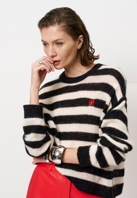 Zwart-wit gestreepte trui in een zachte textuur, met een rood logo accent. Gestyled met een rode leren rok en zilveren armband.