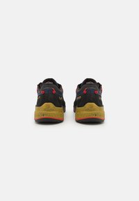 Čierne a námornícke športové topánky majú textúrovaný dizajn, červené akcenty a žltú gumovú podrážku s dezénom. Zadný pohľad ukazuje detail značky.