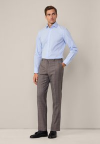 Lichtblauwe gestreepte overhemden met knoopsluiting, gecombineerd met grijs geruite broek. Zwarte nette schoenen maken de outfit compleet.