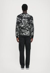 Sweatshirt preto com padrões brancos em espiral, combinado com calças de carga pretas. O tecido parece macio e o design possui gola redonda e punhos canelados.