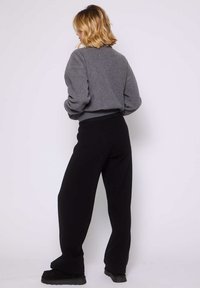 Maglione grigio strutturato con maniche voluminose, abbinato a pantaloni neri a gamba larga. Entrambi i capi presentano un design casual e rilassato.