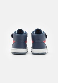 Zapatillas altas azul marino con una raya roja, parte superior sintética, collar acolchado y correa de Velcro. Suela de goma blanca con agarre texturizado.