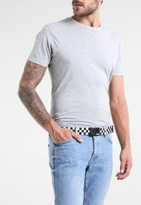 T-shirt grigio in cotone a maniche corte, abbinato a jeans chiari strappati e una cintura quadrata bianco e nera a scacchi, con fibbia rettangolare.