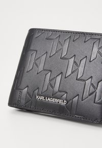 Svart skinnlommebok med et geometrisk hevet mønster, med sølvfarget "KARL LAGERFELD"-logotrykk og glatt tekstur. Kompakt rektangulær design.
