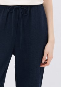 Pantaloni blu navy, con texture e vita elastica regolabile; il tessuto sembra leggero e leggermente stropicciato, con tasche laterali.