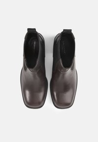 Botas de couro castanho com bicos arredondados, painéis laterais elásticos e alças. Acabamento suave com um brilho subtil, em fundo branco liso.