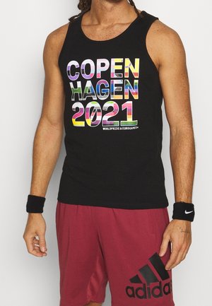 Ærmeløs sort skjorte med farverig tekst "Copenhagen 2021 WorldPride & EuroGames", båret med vinrøde Adidas-shorts og sorte håndledsbind.