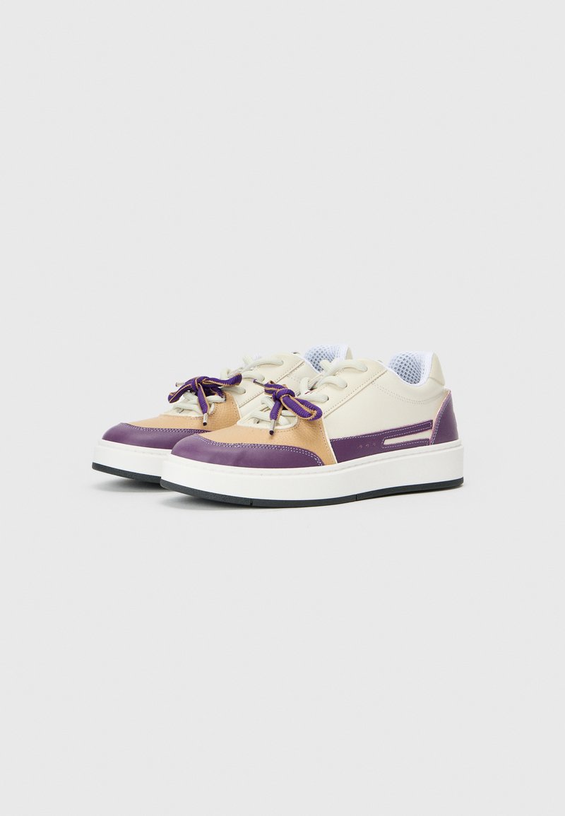 Des baskets avec une tige crème, des accents violets et beiges, des lacets ronds, et une languette en mesh blanc, avec une épaisse semelle blanche et une surface texturée.