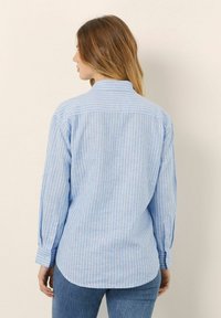 Camicia a righe azzurro chiaro con maniche lunghe, polsini abbottonati, colletto semplice e orlo curvo, realizzata in un tessuto morbido e testurizzato.