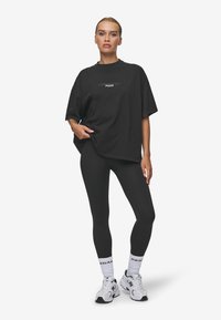 Svart oversize t-shirt med vit grafisk text, tillsammans med svarta leggings och vita sneakers. Slät tyg, avslappnad passform och ankellängd.