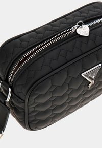 Prešívaná čierna syntetická taška so strieborným zipsom, značkovým srdcovým príveskom a trojuholníkovým logom. Kompaktný a štruktúrovaný dizajn.