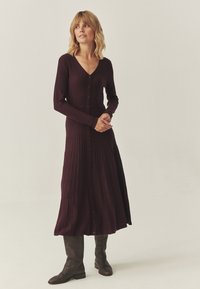 Garšīgs, ribots bordo kleita ar V-veida kakla izgriezumu, garām piedurknēm un pogu aizdari. Apvienota ar brūnām ādas zābakiem līdz ceļiem.