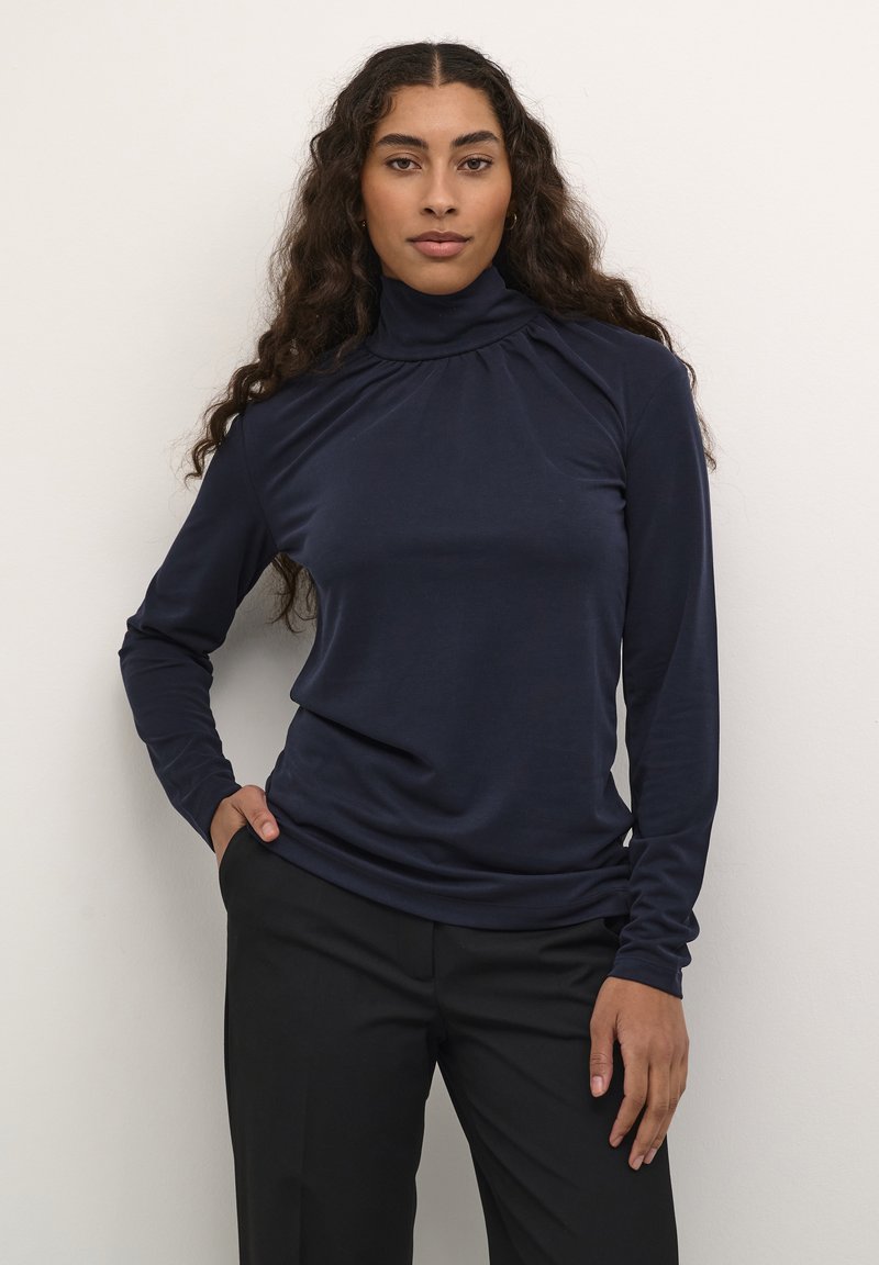 Navy-blaues langärmeliges Rollkragenshirt mit hohem Kragen, weichem Griff und gerafftem Detail am Ausschnitt, kombiniert mit schwarzen Hosen.