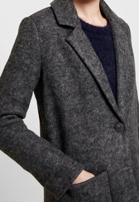 Soprabito grigio in feltro con design strutturato, rever a punta, chiusura con un singolo bottone, due tasche e una texture morbida.
