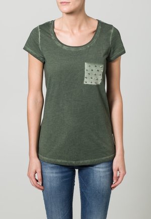 Camiseta de manga corta en color verde oliva, hecha de una tela suave, con un bolsillo frontal decorado con tachuelas plateadas. Cuello redondo y corte relajado.