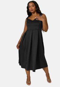 Robe noire sans manches avec un décolleté en V, un corsage ajusté et une jupe plissée ample. Fabriquée en tissu lisse avec une silhouette fluide. Design minimaliste.