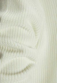 Gros plan sur un tissu tricoté doux de couleur crème avec une texture côtelée et des sections pliées et froncées.