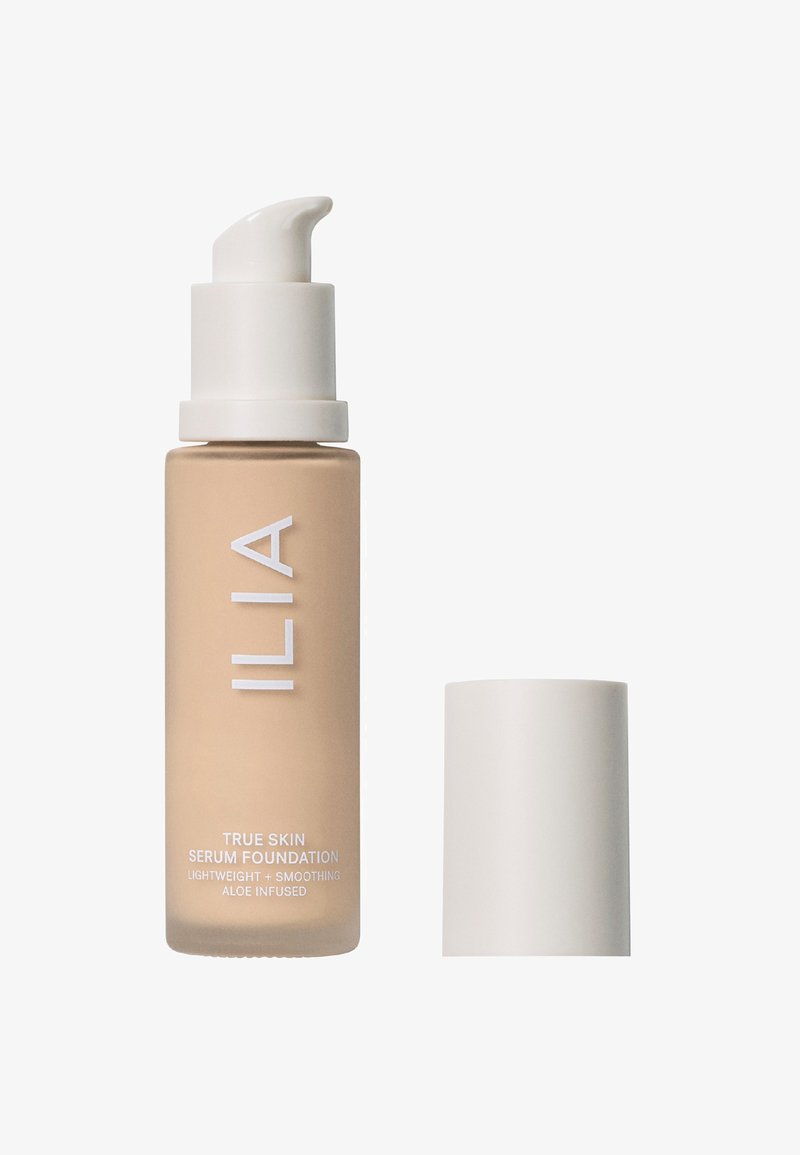 ILIA True Skin Serum Foundation i en glasflaska med beige nyans, vit texturerad pump och matchande lock. Har tydlig etiketttext.