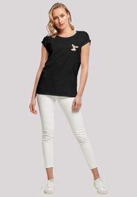 Svart T-skjorte med korte ermer har et lite hundemotiv på venstre bryst, kombinert med hvite skinny jeans og hvite sneakers.