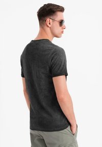 Černé tričko s krátkým rukávem s texturovaným povrchem, kulatým výstřihem a kontrastními černými manžetami, oblečené osobou otočenou zády.