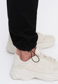 Černé kalhoty s tapered nohavicí, s nastavitelným manžetou a černým šňůrkou. Noste je se světle béžovými sportovními botami.