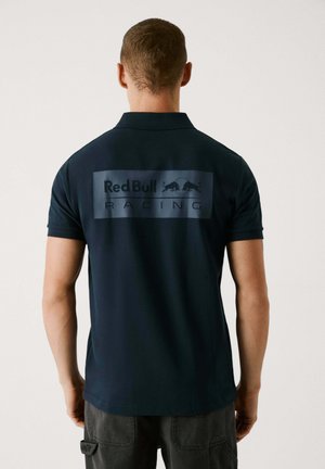 Granatowa koszulka polo z krótkim rękawem, z dużą szaro-czarną wstawką na plecach z napisem "Red Bull RACING" w czerni, wraz z logo oraz gładką teksturą.