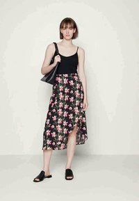Top preto sem mangas com uma saia floral até ao joelho, apresentando flores rosas e brancas sobre um fundo preto, combinada com slides pretos e uma mala preta.