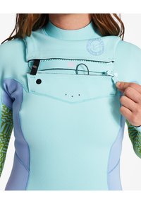 Een lichtblauwe wetsuit met een ritszakje op de borst, met groene geometrische patronen op de mouwen en duurzame stikdetails.