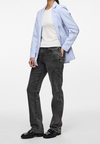 Světle modrý blazer přes bílý přiléhavý top, v kombinaci s tmavě šedými džíny a černými robustními botami. Blazer má propracovaný design a klopové límce.