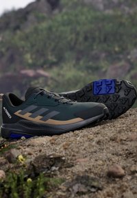 Black and green athletic shoes with a synthetic upper, gray stripes, and a textured rubber sole featuring a blue accent on the heel.