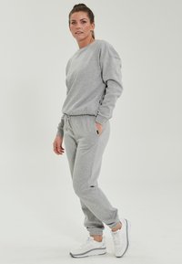 Grå sweatshirt och matchande joggers i mjukt, stretchigt material, med elastisk midja och avrullade anklar. Vita sneakers ingår.