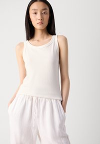 Débardeur blanc à côtes avec un col rond, assorti à un pantalon blanc à cordon de serrage ample. Texture lisse, coupe décontractée, design minimaliste.