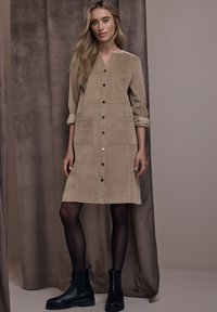 Beige manchesterklänning med V-ringning, långa ärmar, knappstängning framtill och två stora påsydda fickor. Kombinerad med svarta ankelboots.