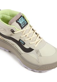 Beige Sneaker mit einem strukturierten Obermaterial, schwarzen und grauen Akzenten, cremefarbenen Schnürsenkeln und einem gepolsterten Schaft. Inklusive Vans-Logo auf der Zunge.