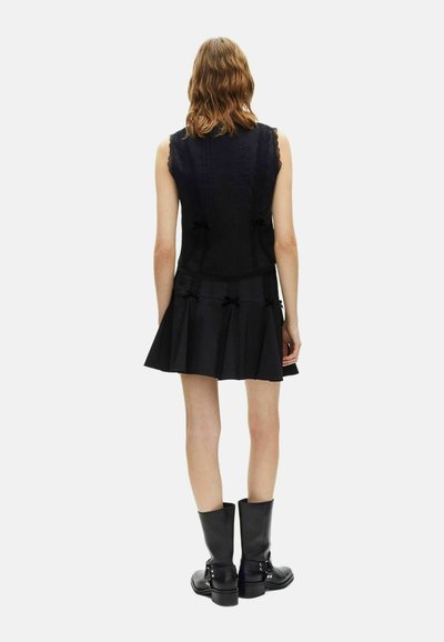 Vestido negro sin mangas con detalles de encaje, falda plisada y cintas. Combinado con botas negras hasta la rodilla con hebillas.