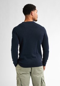 Marinblå stickad tröja med långa ärmar och rund halsringning, med en åtsittande nederkant och mudd, ihop med ljusgröna cargobyxor.