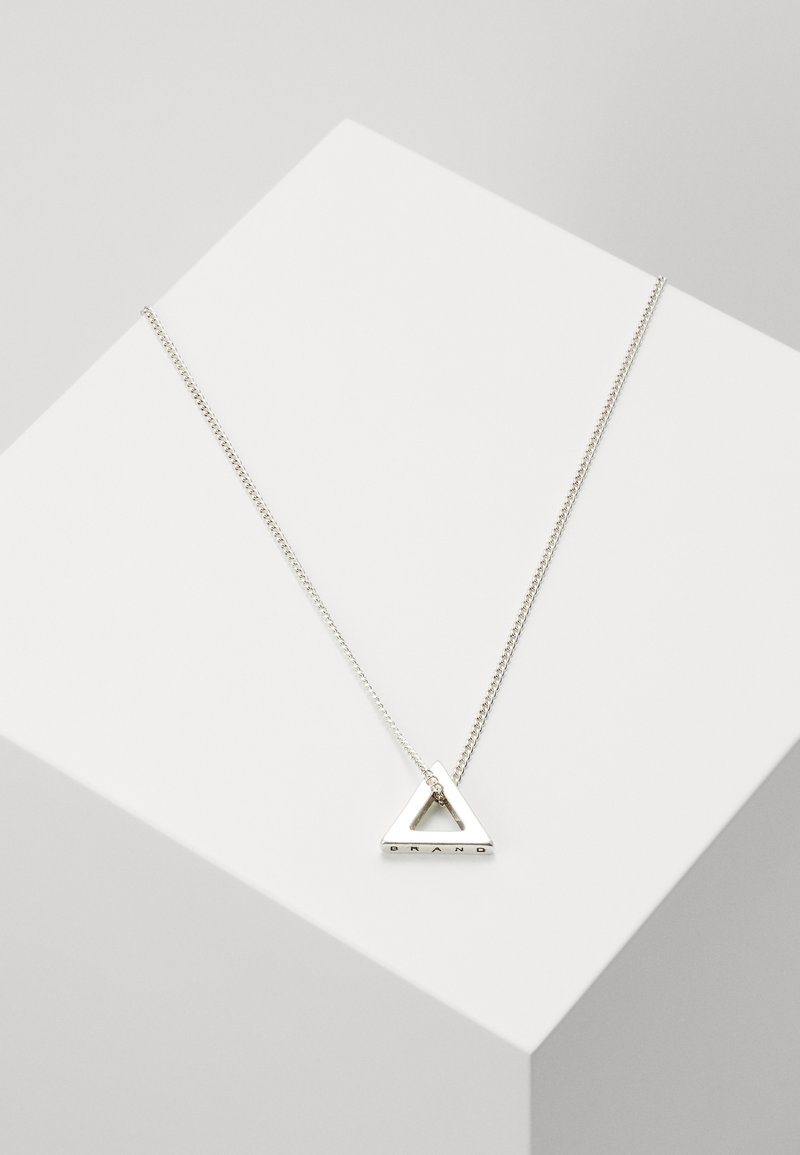 Collier en métal argenté avec un pendentif triangulaire présentant un centre ouvert et un texte gravé. La chaîne est délicate et finement enchaînée.