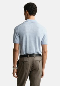Polo shirt bleu clair à manches courtes avec une texture lisse, associé à un pantalon marron texturé et une ceinture noire. Détail subtil du col visible.