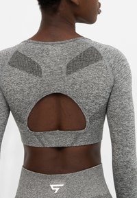 Sivý športový crop top vyrobený z textúrovanej látky, s dizajnom výstrihu na chrbte a sieťovými akcentmi, s dlhými rukávmi.