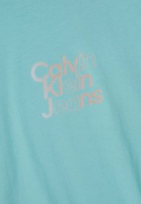 Camiseta de algodón de color azul claro con un logotipo en relieve blanco que dice "Calvin Klein Jeans" en una fuente moderna. Textura suave y lisa.