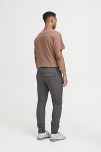 Brown short-sleeve shirt, gray tapered pants with elastic cuffs, and light gray sneakers. Visible back pockets on pants.